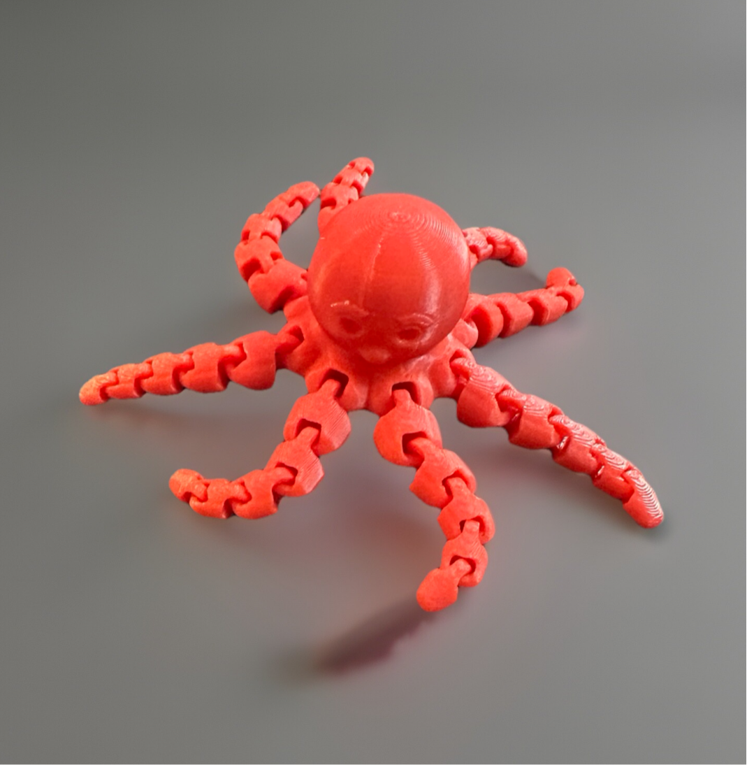 Red 3D articulated fidget octopus toy with flexible jointed tentacles on a gray surface