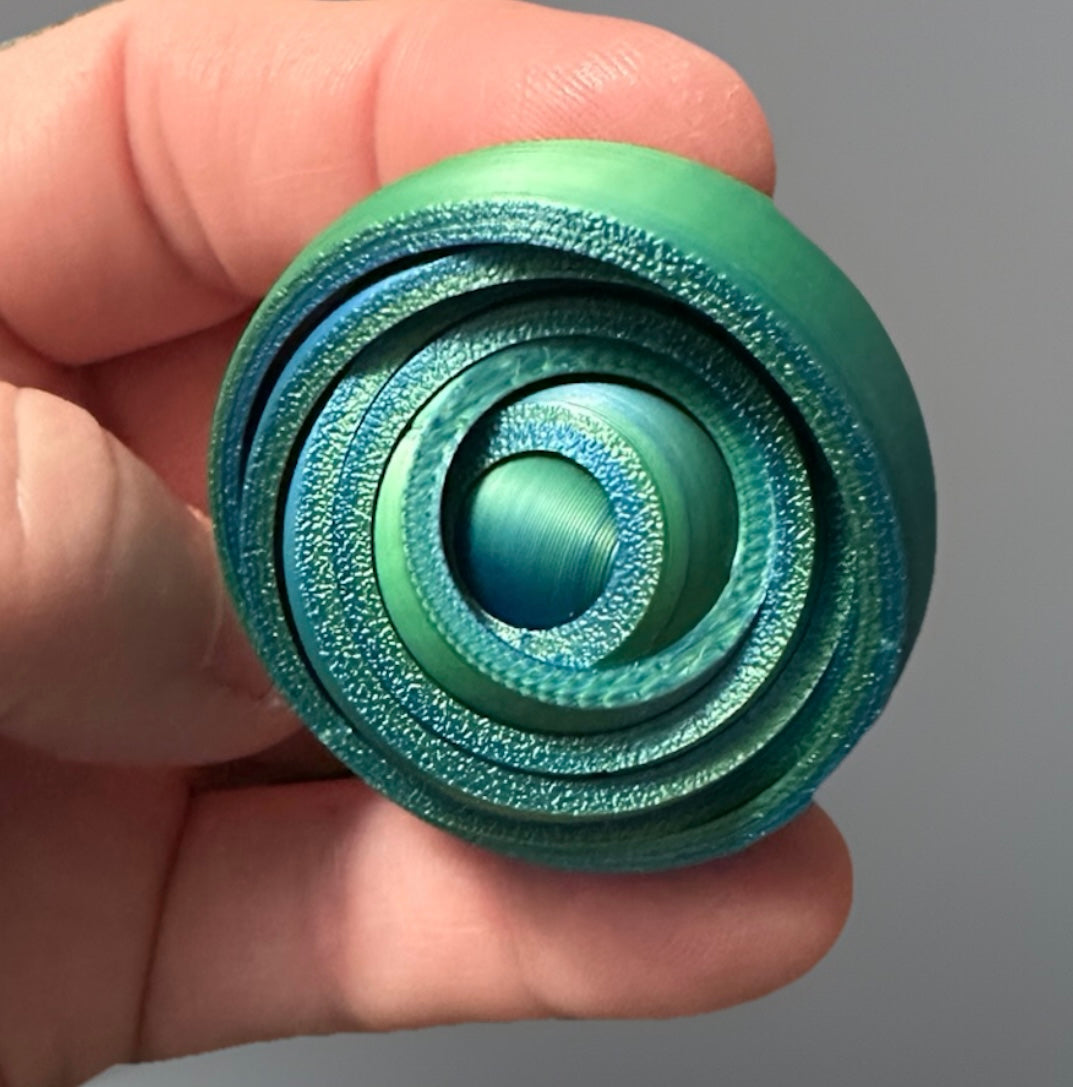Hand holding green and blue 3D gyro fidget spinner with textured concentric rings