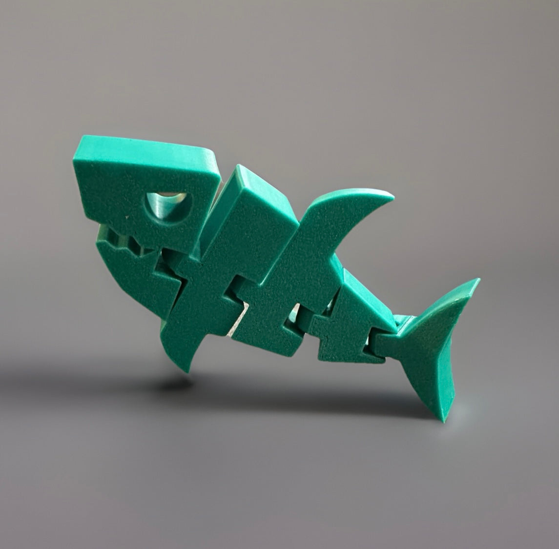 Green articulated shark fidget toy with segmented body and smooth finish on gray background