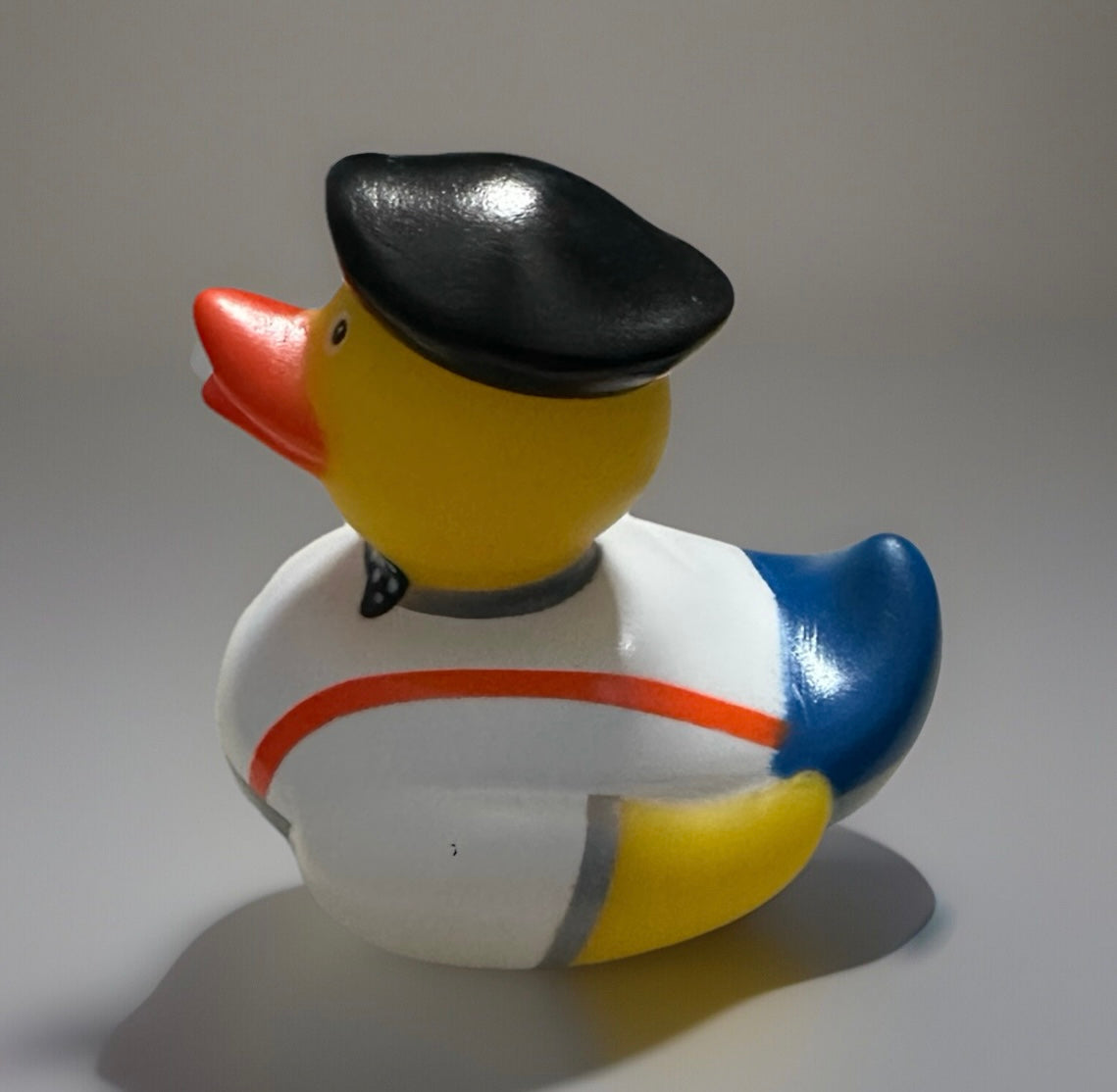 Bow tie rubber duck wearing a black cap with white, blue, and yellow body and orange beak