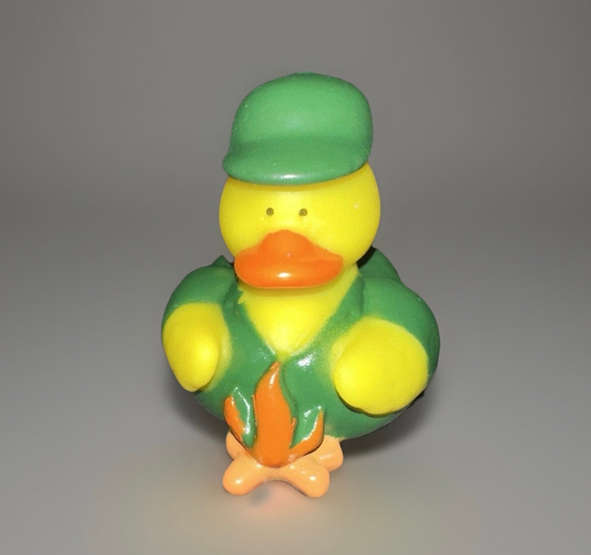 Campfire rubber duck wearing a green hat and jacket sitting by a small campfire