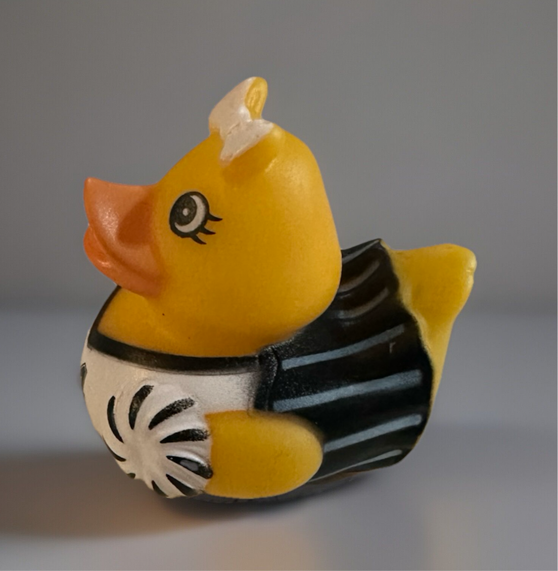 Cheerleader rubber duck toy wearing black and white cheerleading outfit with pom poms