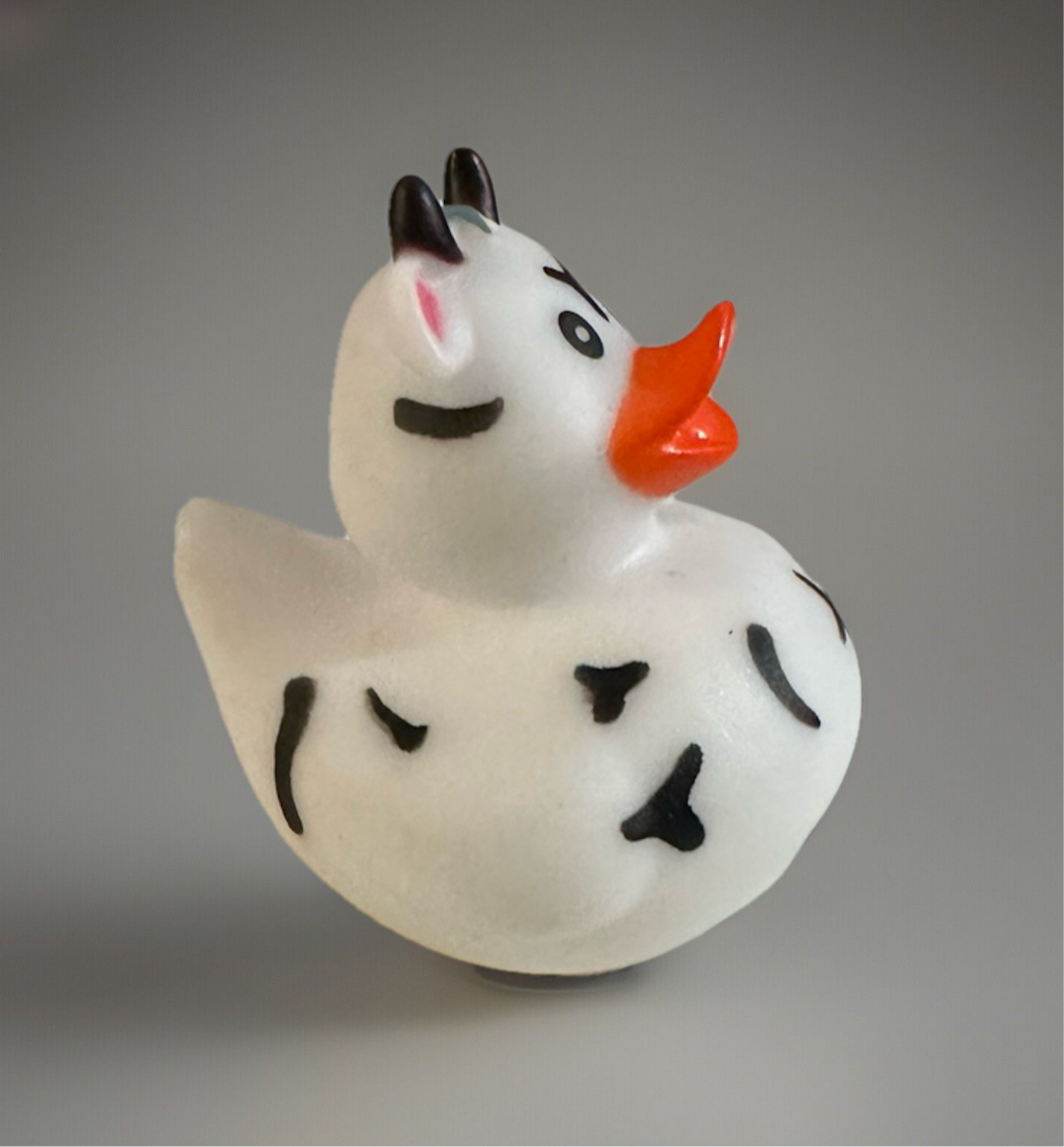 Cow rubber duck with black spots, orange beak, and small black horns on gray background