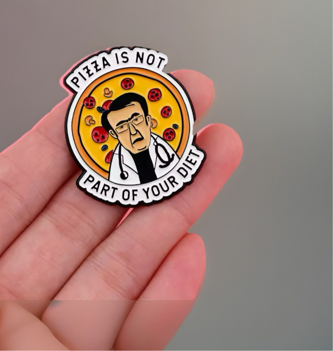 Hand holding a doctor enamel pin with a pizza background and text saying pizza is not part of your diet