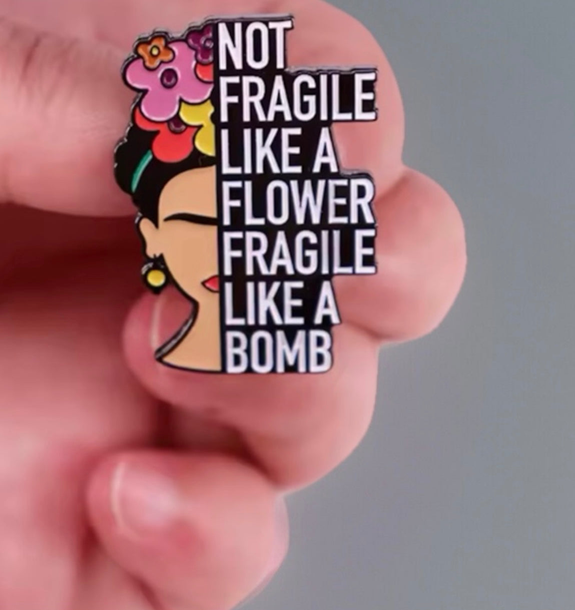 Frida inspired pin featuring colorful flowers and bold text saying not fragile like a flower fragile like a bomb