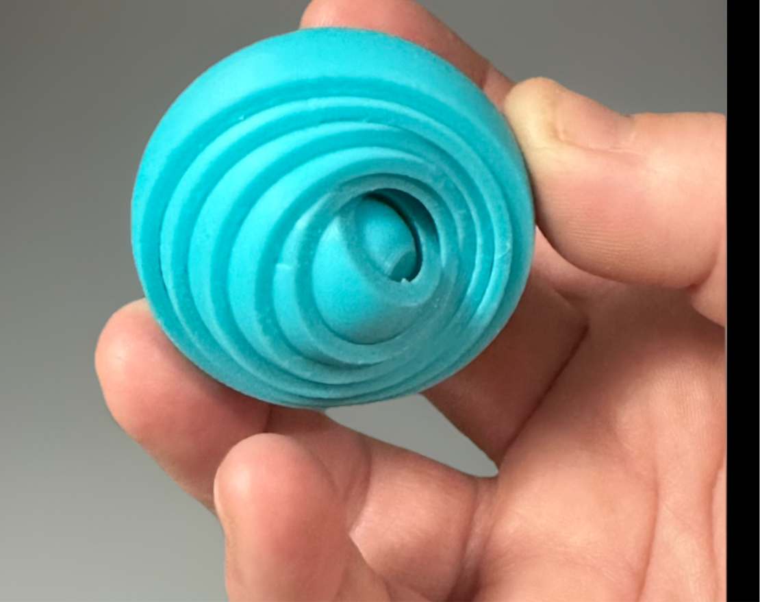 Hand holding a blue 3D gyro finger spinner with concentric circular design for sensory play