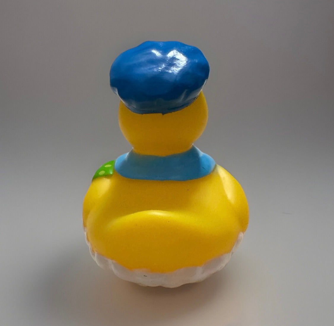 Rear view of a novelty rubber duck wearing a blue hat and collar with a green detail