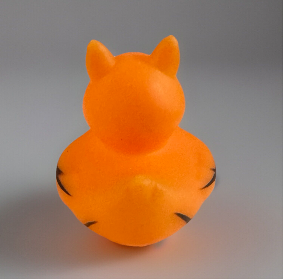 Rear view of orange tiger rubber duck with black stripes and pointed ears on gray background