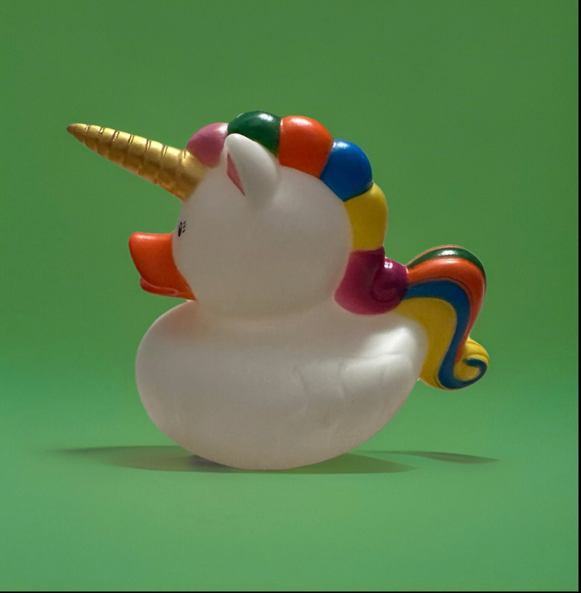 White unicorn rubber duck gift with a golden horn and colorful rainbow mane and tail on green background