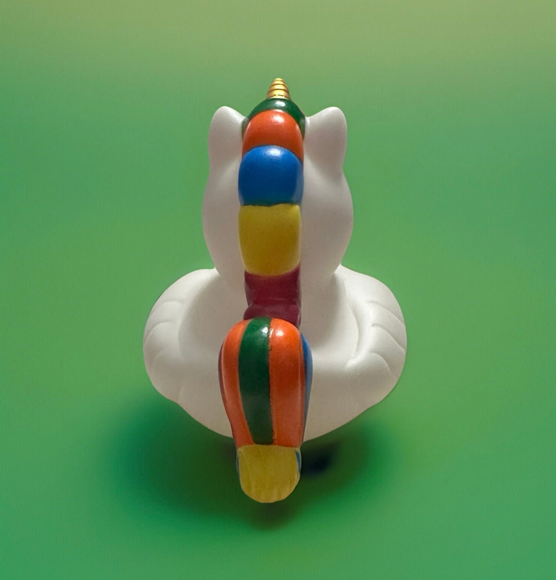 Unicorn rubber duck gift with white body and colorful striped horn and tail on green background