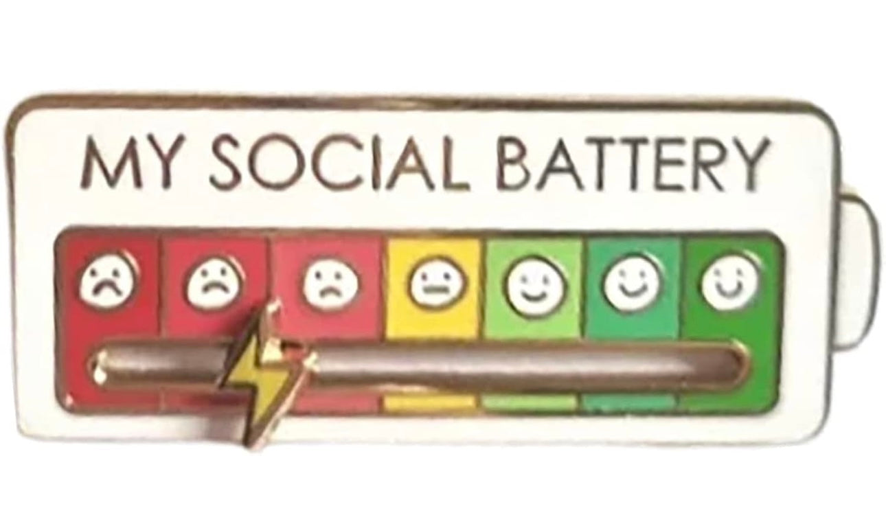 White lapel pin showing a social battery meter with sad to happy faces and a lightning bolt indicator
