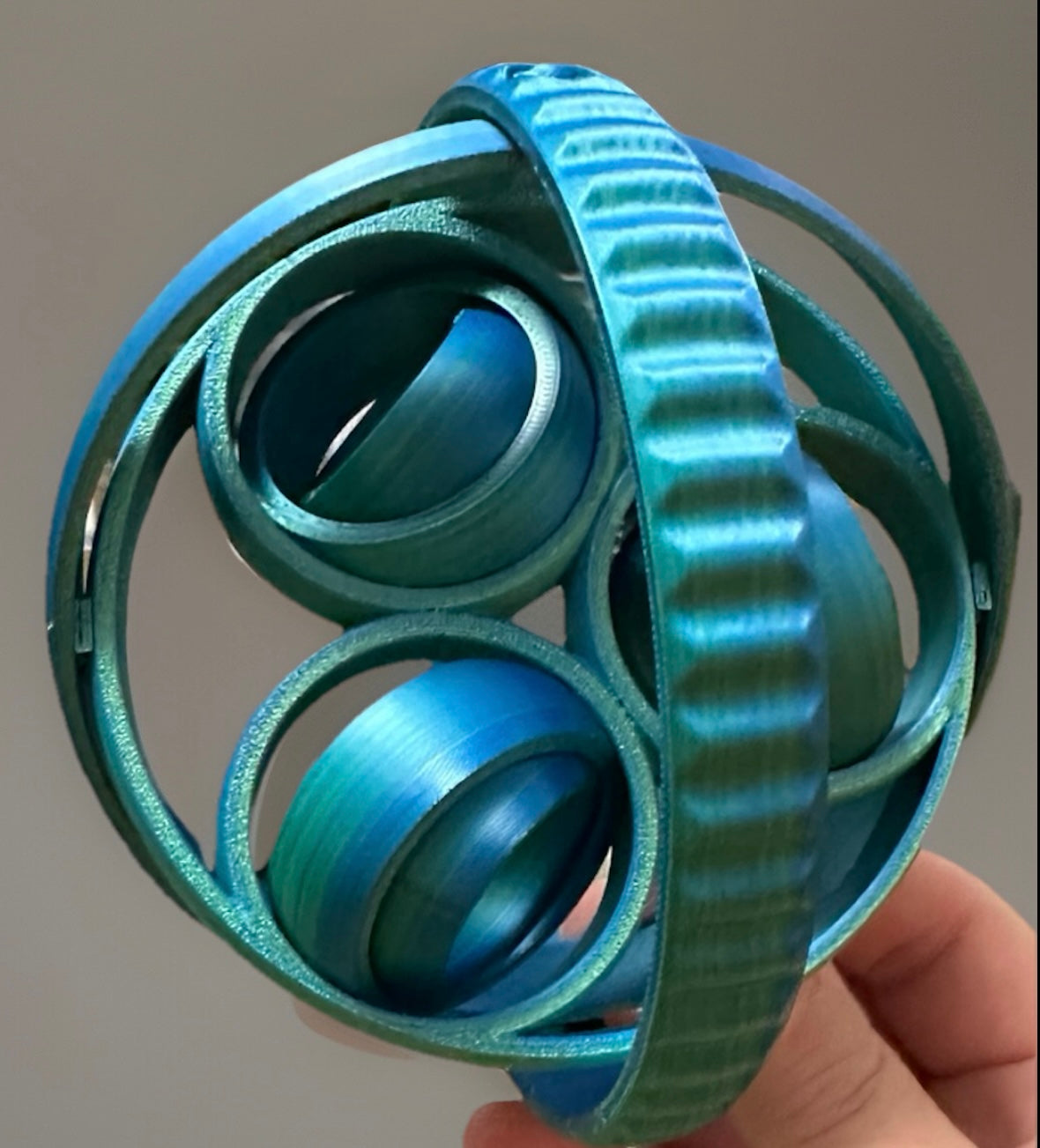 Blue metallic 3D rotating fidget rings held in hand with a smooth textured finish