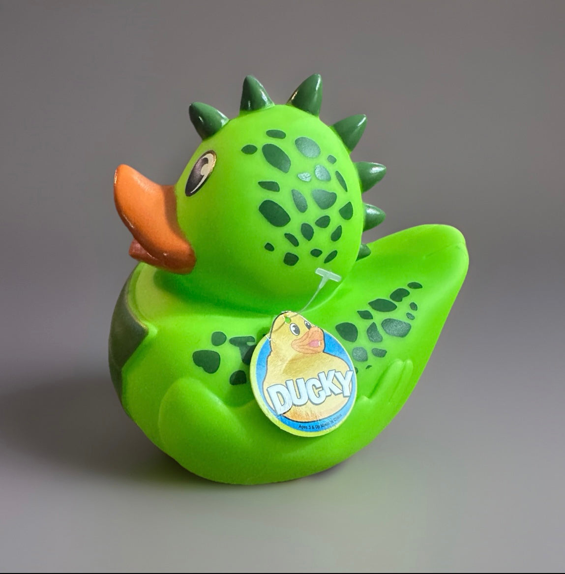Green dinosaur rubber duck with orange beak and dark green spots and spikes from Reed’s Rubber Ducks
