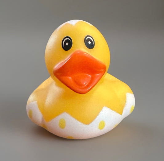 Yellow Easter egg rubber duck with orange beak and white spotted egg pattern sitting on gray background