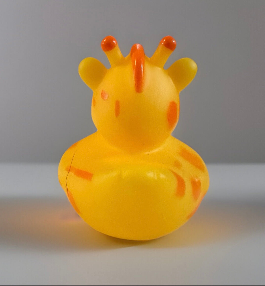 Yellow giraffe rubber duck toy with orange spots and orange horns on gray background