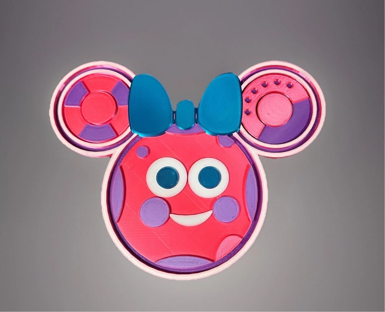 Colorful Oh Quoodles figure with blue bow and playful facial features in pink and purple tones