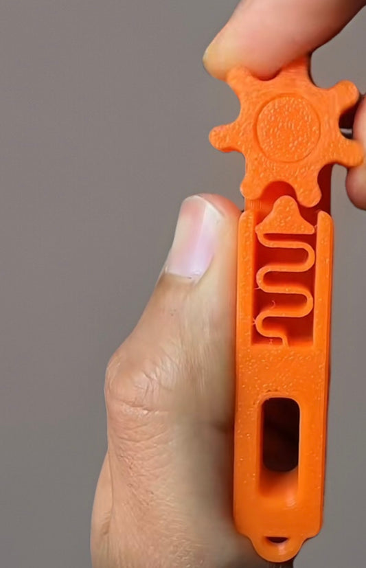 Orange 3D printed fidget keychain held between fingers showcasing tactile maze design