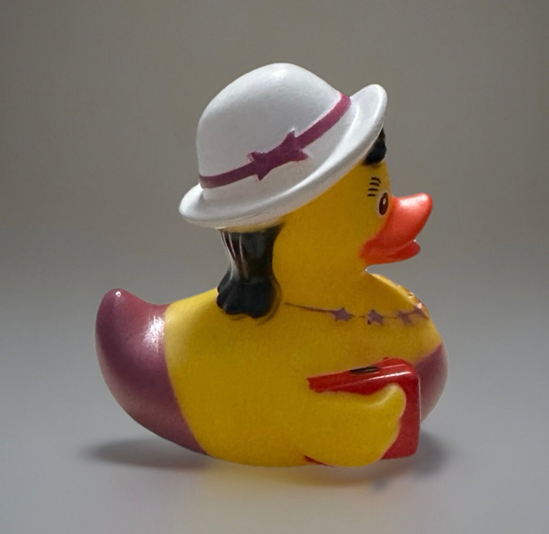 Party girl rubber duck wearing white hat with purple band and holding a red purse