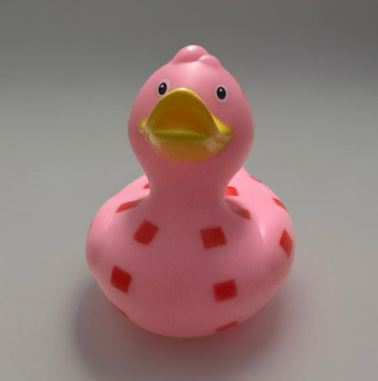 Pink checkered rubber duck with yellow beak and red square patterns on a smooth surface