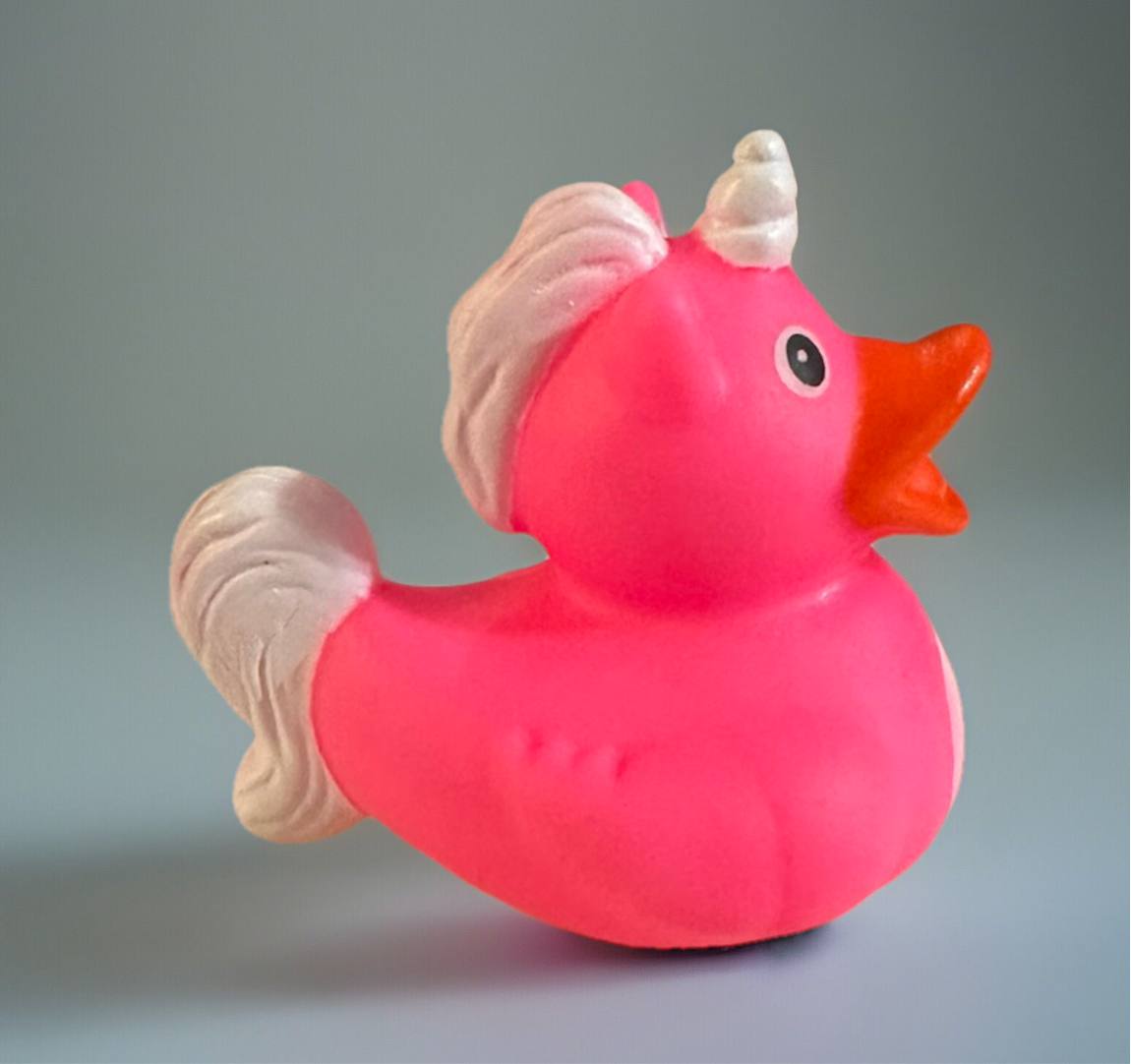 Pink unicorn rubber duck with white horn and mane and orange beak on gray background