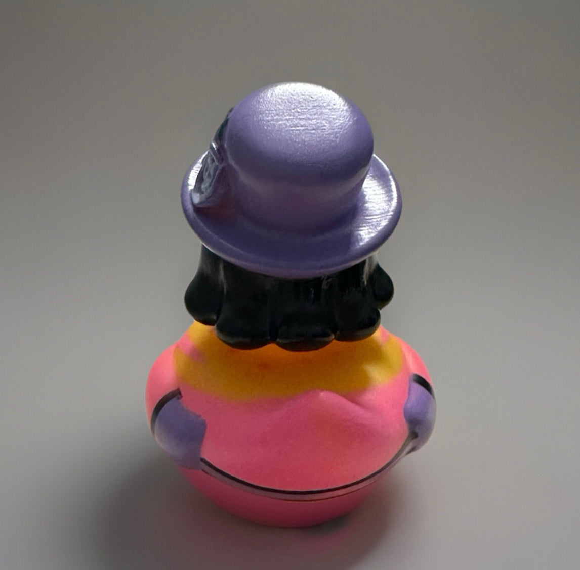Rear view of purple top hat rubber duck with black hair and colorful pink and yellow body