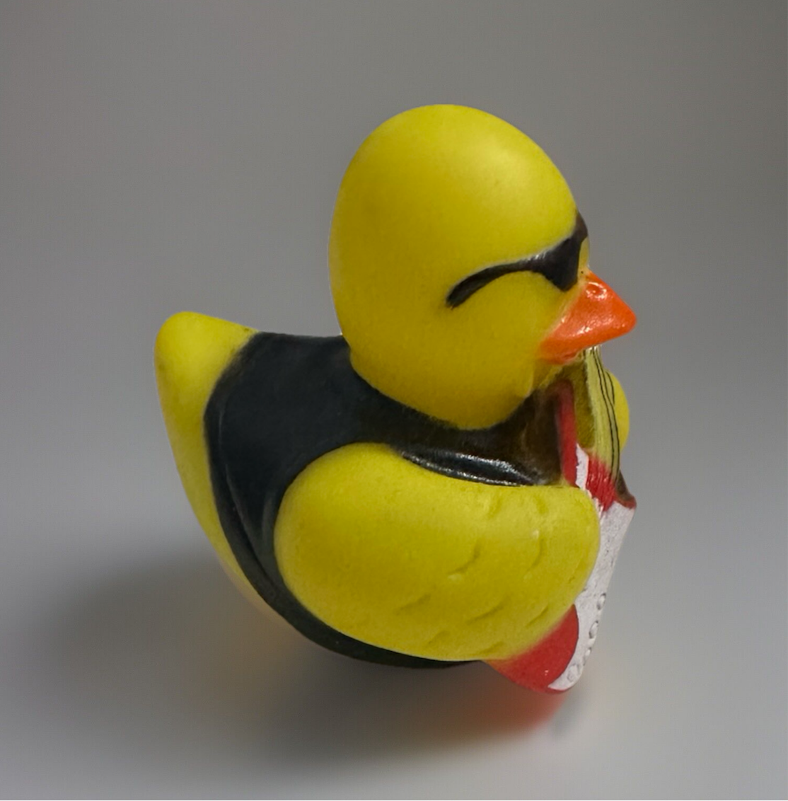 Yellow rock and roll rubber duck wearing sunglasses and black vest holding red and white guitar